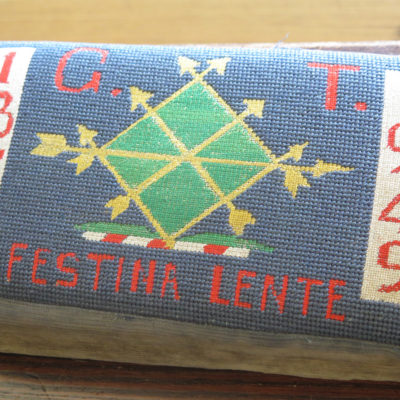 besticktes Kissen mit Wappen drauf und der Text: Festina Lente
