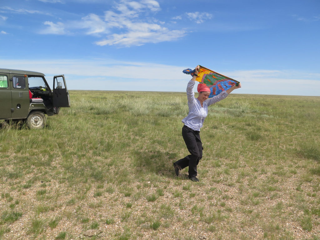 Links ein russischer Bus, blauer Himmel und Gras, Frau spielt mit Tuch im Wind