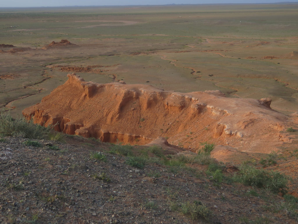 Rote Klippen Bayanzag in der Mongolei, dahinter Steppenlandschaft