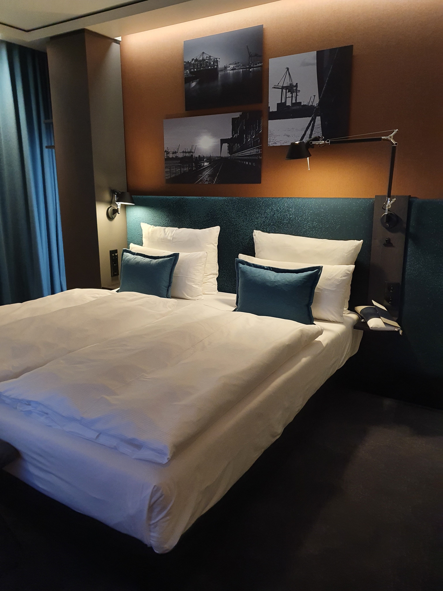 Motel One Hamburg Hotelzimmer. Doppelbett mit blaue Kissen. An der Wand schwarz-weißbilder von hamburg
